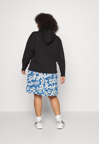 Sweatshirt com capuz preto combinado com um vestido floral azul. O vestido apresenta flores brancas, é até ao joelho e tem uma cintura elástica. Ténis brancos visíveis.
