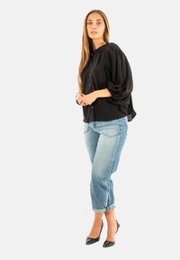 Blusa nera a maniche a sbuffo con chiusura a bottoni, abbinata a jeans azzurri con risvolto e décolleté neri a punta. Tessuto dal tatto morbido.