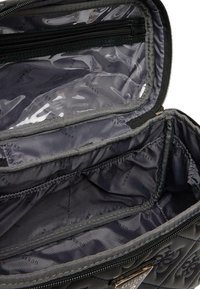 Bolso de mano negro acolchado con un interior brillante que cuenta con múltiples compartimentos y un cierre de cremallera, detallado con el logo "GUESS" en toda su superficie.