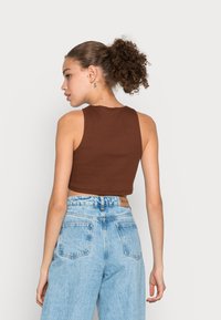 Top cropped ribbed castanho com um design ajustado, combinado com jeans de cintura alta azul claro, apresentando uma vista traseira do conjunto.