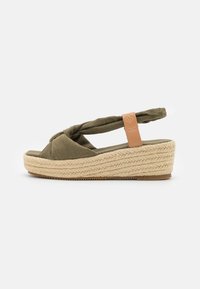 Olive green espadrille sandal with a knotted fabric upper, woven jute platform, and a tan leather accent on the heel strap.