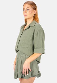 Robe en coton texturé vert avec un haut de chemise col et ourlet froncé. Comprend une poche poitrine unique et des manches retroussées.
