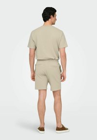Beige tekstureret sæt bestående af en kortærmet bluse og shorts, med elastisk talje og baglommer, parret med afslappede sneakers.