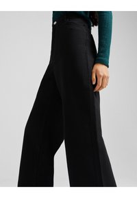 Pantalones anchos de color negro, confeccionados con una tela suave. Presentan una cintura alta con cierre de botón y bolsillos laterales. Acentuados por líneas limpias.