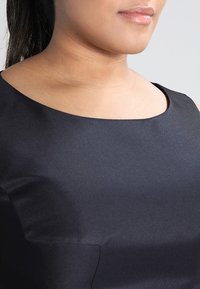 Svart ärmlös klänning med rund halsringning, med slät satin tyg och en subtil fickdetalj på framsidan.