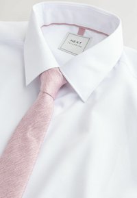 Biała koszula z materiału o fakturze i różowym krawacie. Kołnierzyk jest sztywny, a koszula ma subtelny wzór. Metka głosi "NEXT Tailoring".