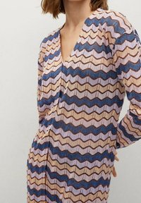 Cardigan en tricot avec un motif en zigzag dans des nuances de rose, bleu et marron, avec un décolleté en V profond et des manches longues. Tissu texturé.