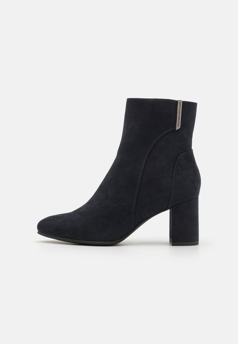 Bottine en daim bleu foncé avec un bout légèrement pointu et un talon bloc épais. Elle présente une couture latérale et un discret accent métallique à l'arrière.