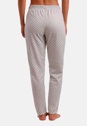 Personne sans haut portant un pantalon gris clair avec un petit motif géométrique répétitif, debout pieds nus sur un fond blanc.