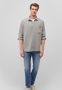 Gray long-sleeve button-up shirt with a chest pocket, paired with blue jeans. The fabric has a subtle texture. White t-shirt underneath, light footwear.