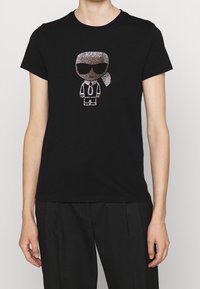 Svart bomullströja med en förstärkt cartoonfigur prydd med strass, som bär solglasögon, slips och hästsvans, stylad i vita och silver detaljer.