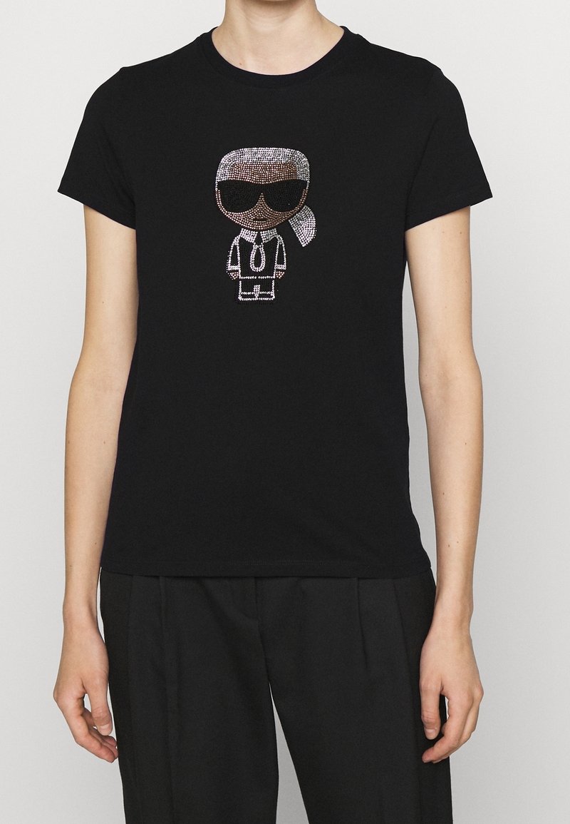 Svart bomullströja med en förstärkt cartoonfigur prydd med strass, som bär solglasögon, slips och hästsvans, stylad i vita och silver detaljer.