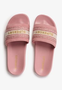 Sandalias de playa rosas con una correa texturizada que presenta un patrón blanco y rosa, y el logo dorado "Superdry". Suela y interior de goma suave.