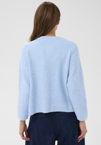 Gai zilgani ribota džemperis ar garām piedurknēm un apaļu kakla izgriezumu; mīksta tekstūra; īsāka muguras mala, apvienots ar tumšiem džinsiem.