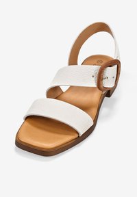 Sandalia de cuero blanco con dos correas anchas, diseño de punta cuadrada y una hebilla de madera marrón. Plantilla acolchada y suela baja marrón.