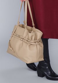 Beige leren handtas met een zachte textuur, een geraffineerd ontwerp en contrasterend beslag. Beschikt over twee lange handvatten en een verstelbare schouderband.