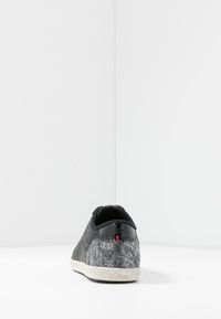 Baskets noires avec un dos en feutre gris texturé, des détails en cuir noir lisse, une semelle en caoutchouc, et des accents de logo subtils en rouge et bleu.