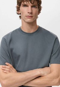 Harmaa lyhythihainen t-paita pehmeästä, sileästä kankaasta. Pyöreä pääntie ja klassinen leikkaus ilman näkyviä logoja tai kuvioita.