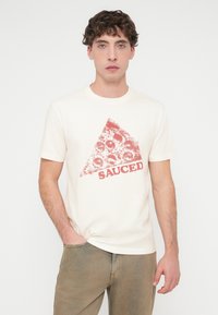 Μπλούζα από βαμβάκι σε κρεμ απόχρωση με κόκκινο γραφικό μιας φέτας πίτσας και τη λέξη "SAUCED" τυπωμένη από κάτω. Μανίκια κοντά και λαιμόκοψη τύπου crew.