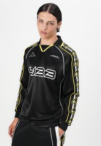 Fekete, hosszú ujjú sportmez sárga kiegészítőkkel és fehér díszítéssel. A elején a "433" felirat, a mellkason és az ujjakon a Kappa logó található.