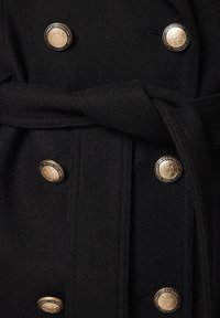 Czarny wełniany płaszcz z podwójnym zapięciem i złotymi guzikami. W zestawie pasujący materiałowy pasek oraz miękka faktura.