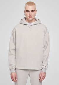 Lys grå, oversized hoodie lavet af blødt stof med en forhåndskangaroo lomme. Har en hætte med snøre og ribbede manchetter.