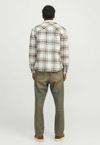 Geruite flanellen blouse in wit, bruin en tan met een kraag, lange mouwen en knoopmanchetten, gecombineerd met olijfgroene jeans en bruine schoenen.