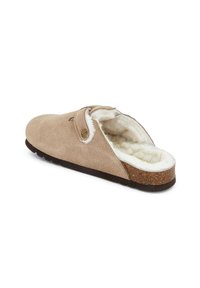 Ciabatta beige in suede con una morbida fodera di pelliccia bianca, suola in sughero e un accento con bottone sul lato, progettata per comfort e calore.