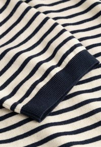 Bela tkanina z enakomerno razporejenimi horizontalnimi mornarsko modrimi črtami in mornarsko modrim rebrastim manšetom.