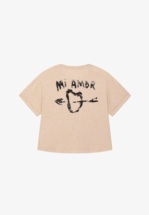 T-shirt beige à manches courtes avec un design graphique noir portant le texte "Mi Amor" et un motif de flèche au dos, coupe décontractée.