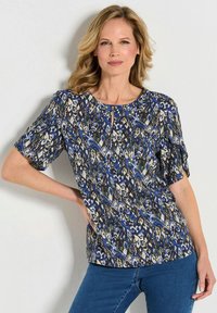 Blau gemusterte Bluse mit kurzen Ärmeln, Rundhalsausschnitt und einem Schlüsselaugen-Detail. Enthält eine Mischung aus Texturen in einem lebhaften Design.