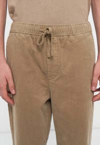 Light brown corduroy pants with an elastic waistband and drawstring. Features side pockets and a soft, textured finish.