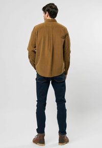 Brun fløjlsskjorte med bagåge, lange ærmer og knapmanchetter, parret med mørkeblå slim-fit jeans og brune støvler.