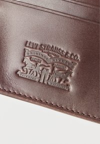 Καφέ δερμάτινη ετικέτα Levi Strauss & Co. με ανάγλυφη απεικόνιση δύο αλόγων που τραβούν το τζιν και κείμενο που περιλαμβάνει «Original Riveted Quality Clothing.»