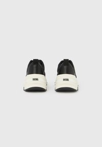 Ζευγάρι μαύρα αθλητικά παπούτσια Diesel, εμφανιζόμενα από πίσω, με λευκές χοντρούς σόλες και θηλιές έλξης, σε απλό γκρι φόντο.