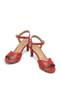 Czerwone skórzane sandały na słupku, z krzyżującymi się paskami i paskiem wokół kostki. Gładka tekstura i otwarty nos.