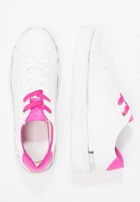 Bílé tenisky s růžovými akcenty a metalickými detaily. Šňůrky jsou jasně růžové, gumové podrážky jsou bílé a jazyk je vyrobený z růžového materiálu, který připomíná kůži.