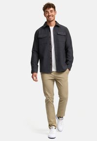 Dark gray button-up shirt with two chest pockets, paired with khaki pants and white sneakers. Casual design with a smooth texture.