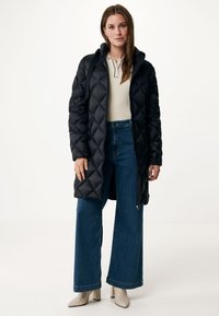 Zwarte gewatteerde lange pufferjas met een capuchon, voorzien van een ritsluiting en zijzakken. Het model combineert het met wide-leg blauwe jeans.