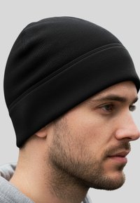 Uomo con barba corta che indossa un berretto nero di maglia e una felpa leggera grigia, che guarda a destra su uno sfondo grigio chiaro uniforme.