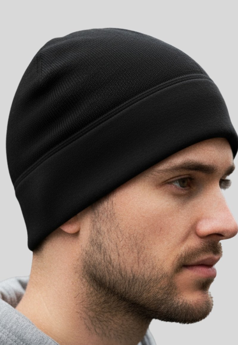 Uomo con barba corta che indossa un berretto nero di maglia e una felpa leggera grigia, che guarda a destra su uno sfondo grigio chiaro uniforme.