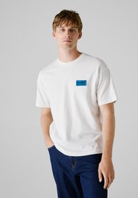 Witte katoen t-shirt met een blauw geborduurd "Red Bull Racing" logo op de linkerborst. Korte mouwen en een ronde hals.