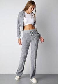 Gray cropped hoodie with a zipper, paired with gray sweatpants featuring side stripes. Worn with white sneakers, creating a cohesive athleisure look.