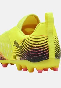 Scarpino da calcio giallo con upper testurizzato, caratterizzato da un design a gradiente nero e rosa, logo distintivo e tacchetti multicolori per una migliore aderenza.