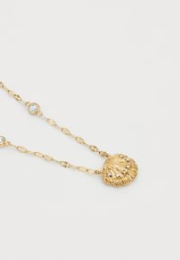 Gouden ketting met een schelp-hanger met gestructureerde ribbels en kleine, heldere versieringen. De ketting heeft een afwisselend schakelontwerp.
