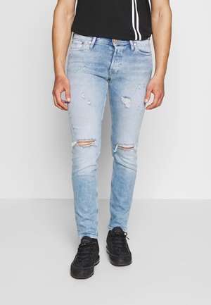 Jeans skinny bleu clair avec des détails déchirés, y compris des genoux déchirés et des bords effilochés, en tissu denim. Portés avec des baskets noires.