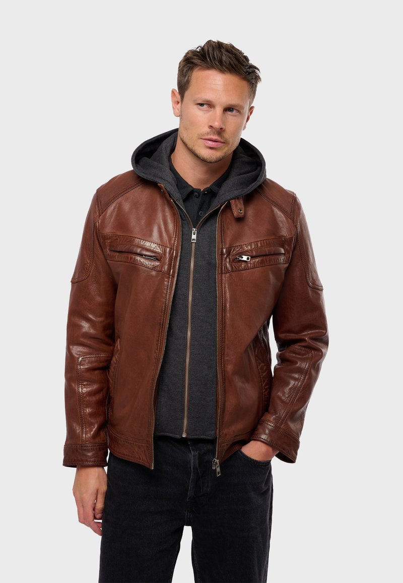 Bruine leren jasje met een gladde textuur, rits aan de voorkant, twee borstzakken en een staande kraag. Draag het over een grijze hoodie en donkere spijkerbroek.
