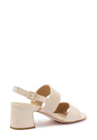 Sandali con tacco in suede beige con due cinghie incrociate, una cinghia alla caviglia regolabile con fibbia dorata e un tacco spesso.