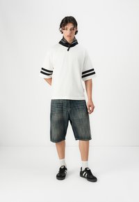 Hvid oversized t-shirt med sorte striber, afslappede denim shorts. Sorte sneakers med hvide striber, sort bandana om halsen.