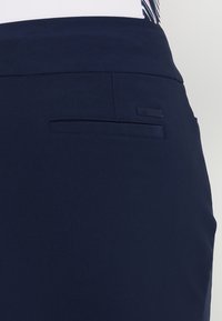 Navy blue skirt with a smooth texture, featuring a single back pocket and a small brand label accent. Simple design, tailored fit.